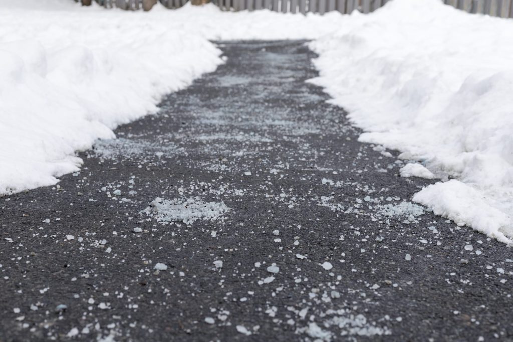Asphalt sidewalk with a cleared path and scattered salt crystals